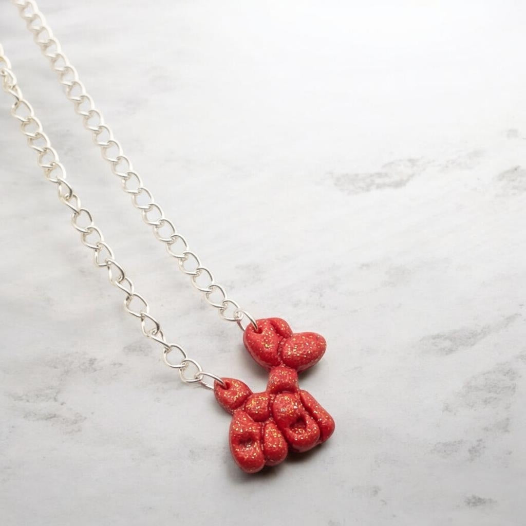 Sparkling red balloon dog necklace on a pink background