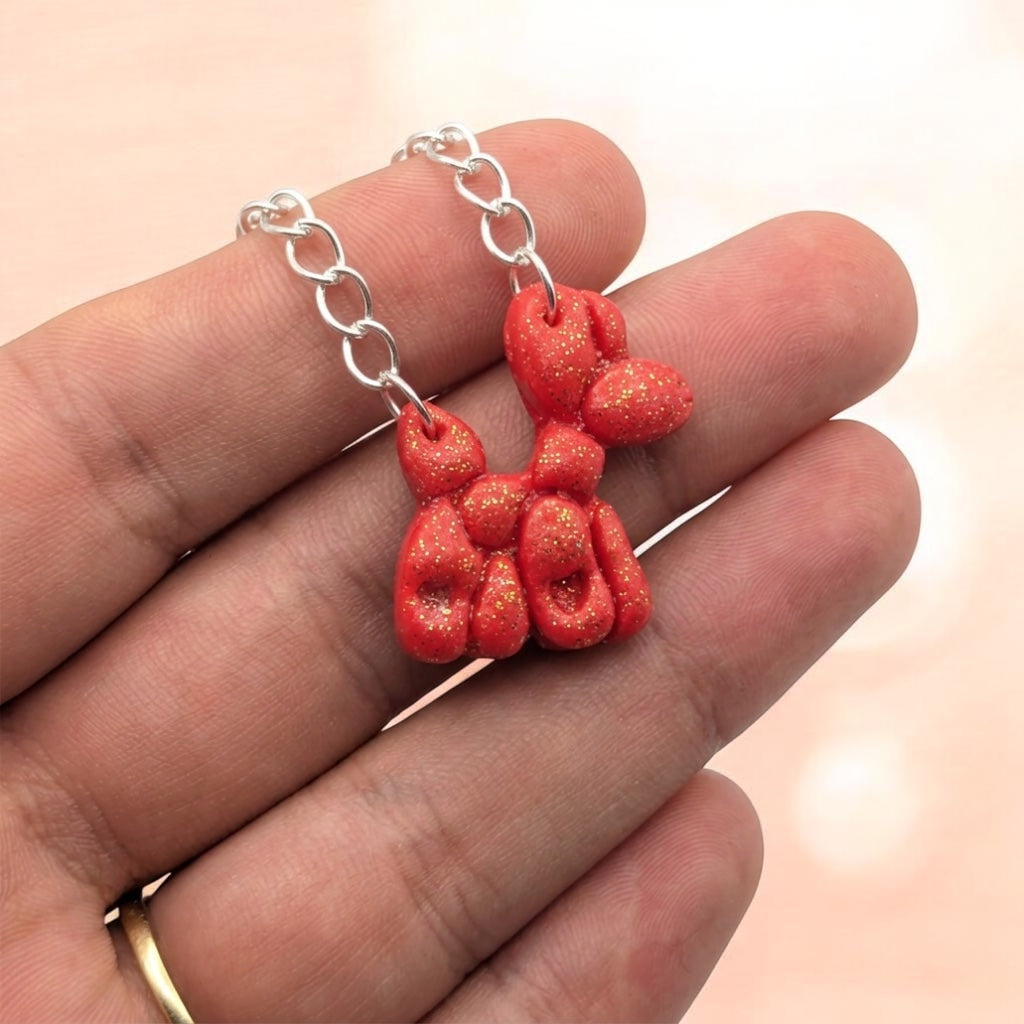 Sparkling red balloon dog necklace pendant held in a hand