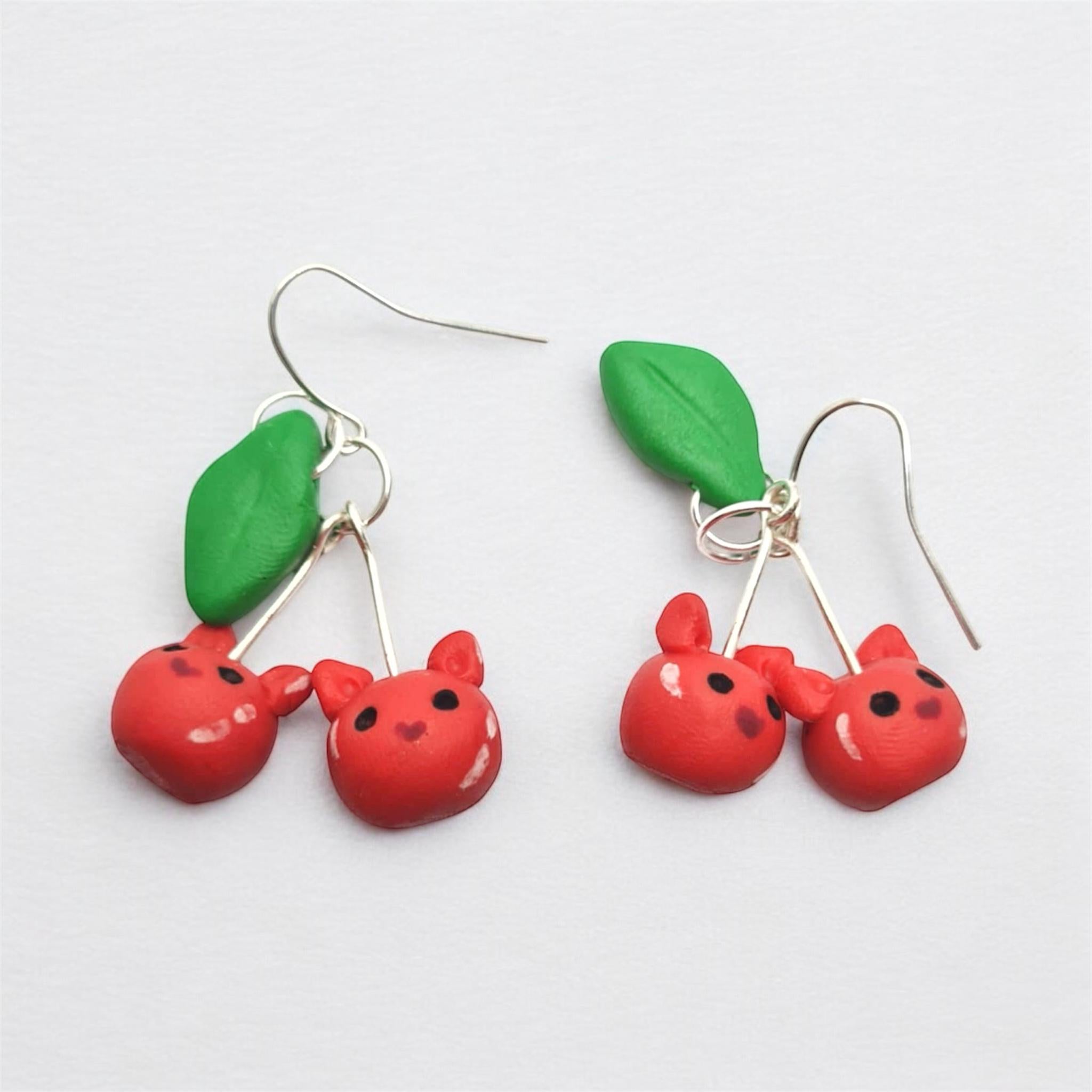 Cherry-themed earrings with red cherries and green leaves on a white background