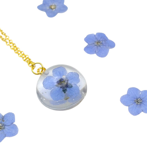 Necklace with a clear pendant featuring blue flowers, surrounded by additional blue flowers on a white background.