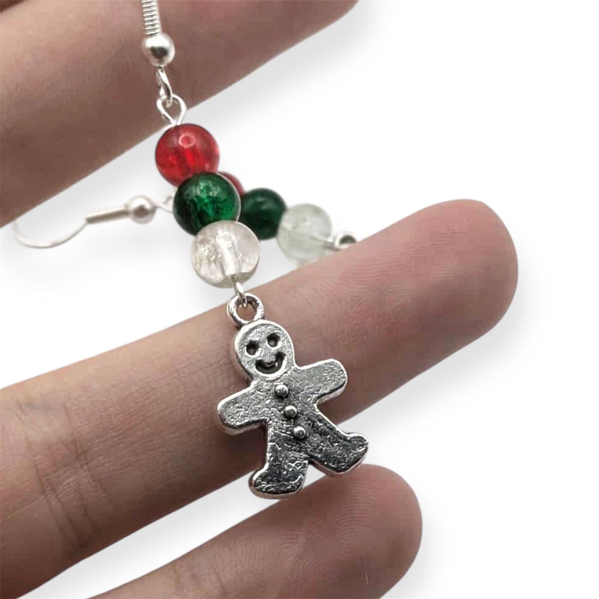 Gingerbread man earring with colorful beads on a finger against a white background