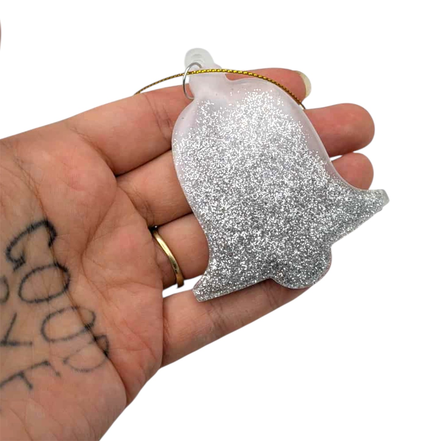 Silver glittery bell ornament held in a hand with tattoos on a white background