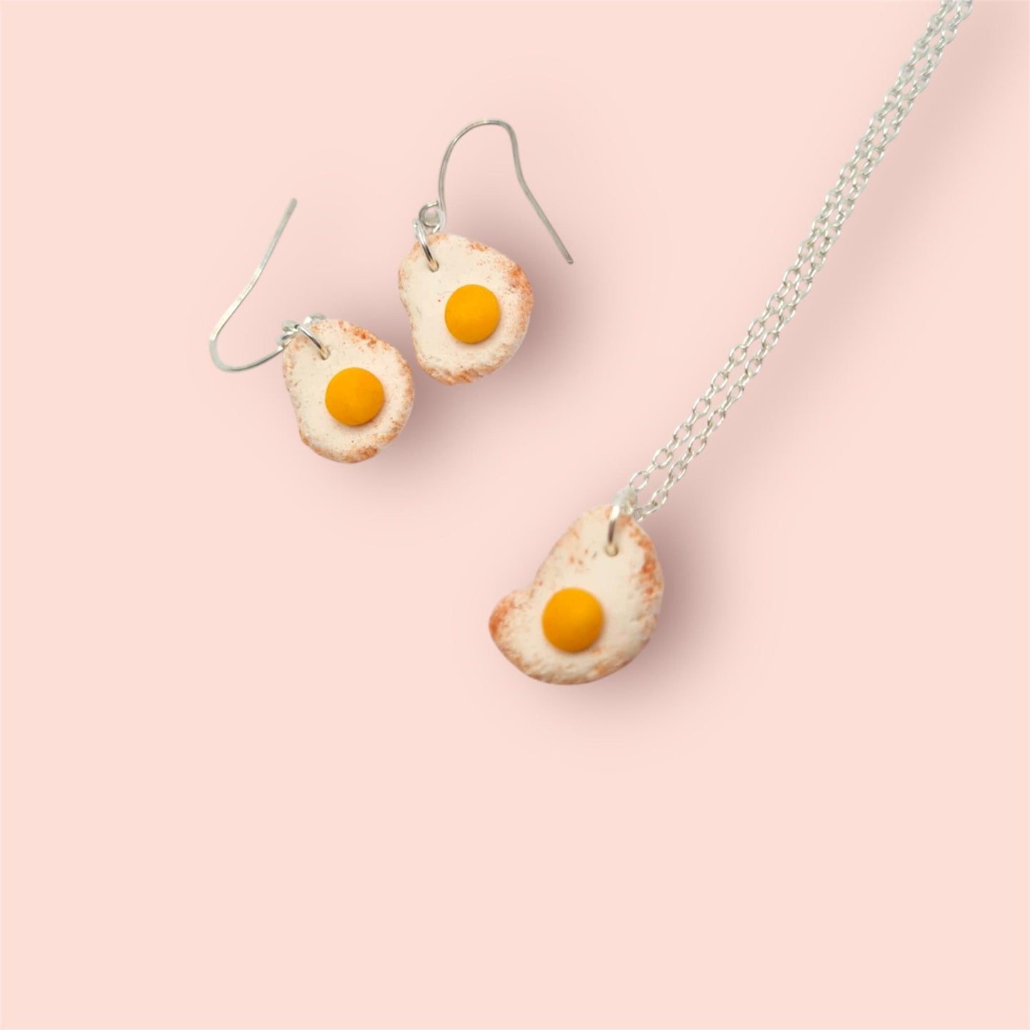 Egg-shaped earrings and necklace on a pink background