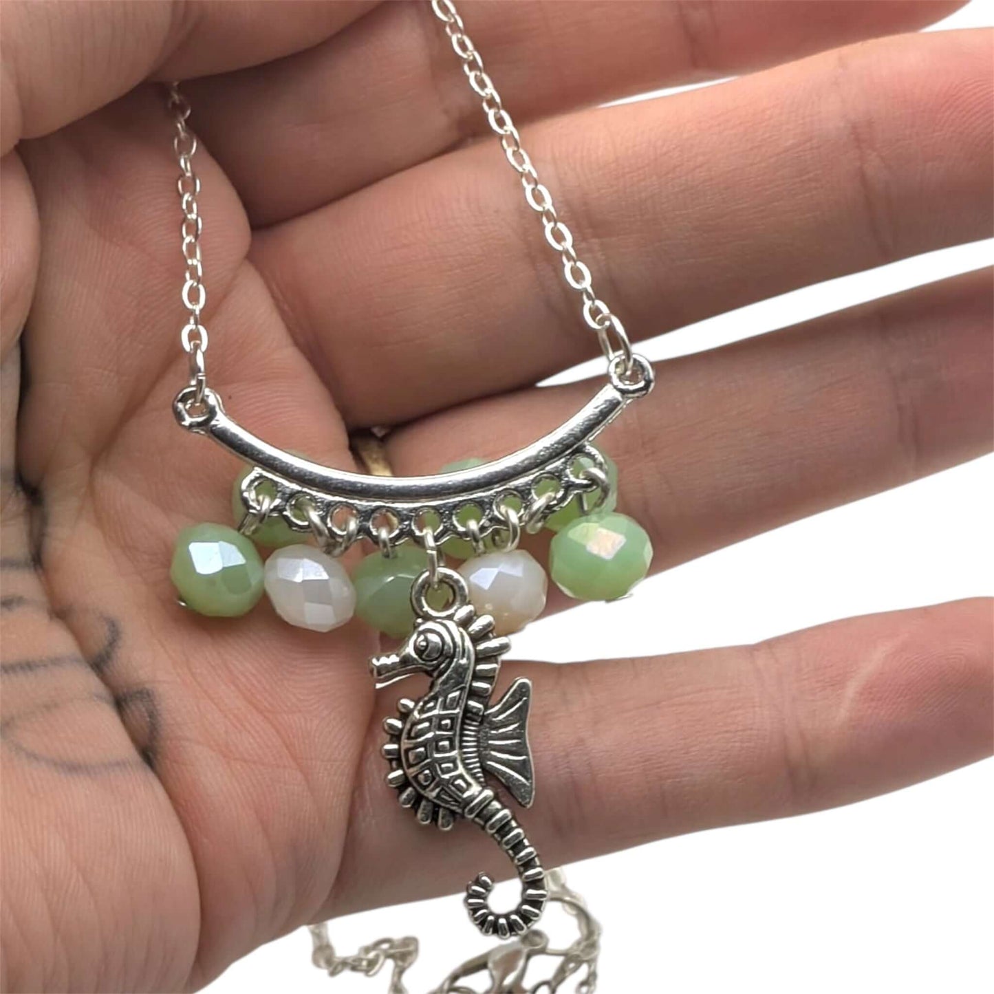 Seahorse necklace held in hand showing a silver animal pendant on white background 