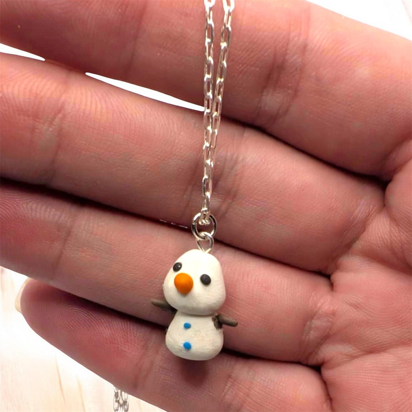 Small snowman charm on a chain held in a hand