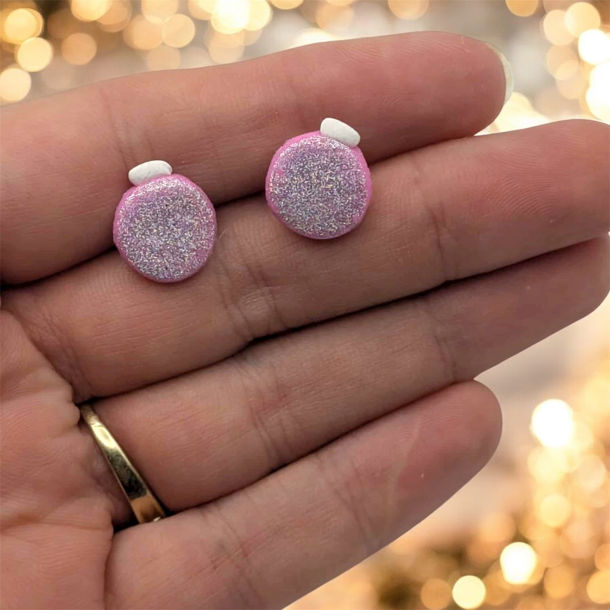 Pink glittery earrings held between fingers with a blurred light background