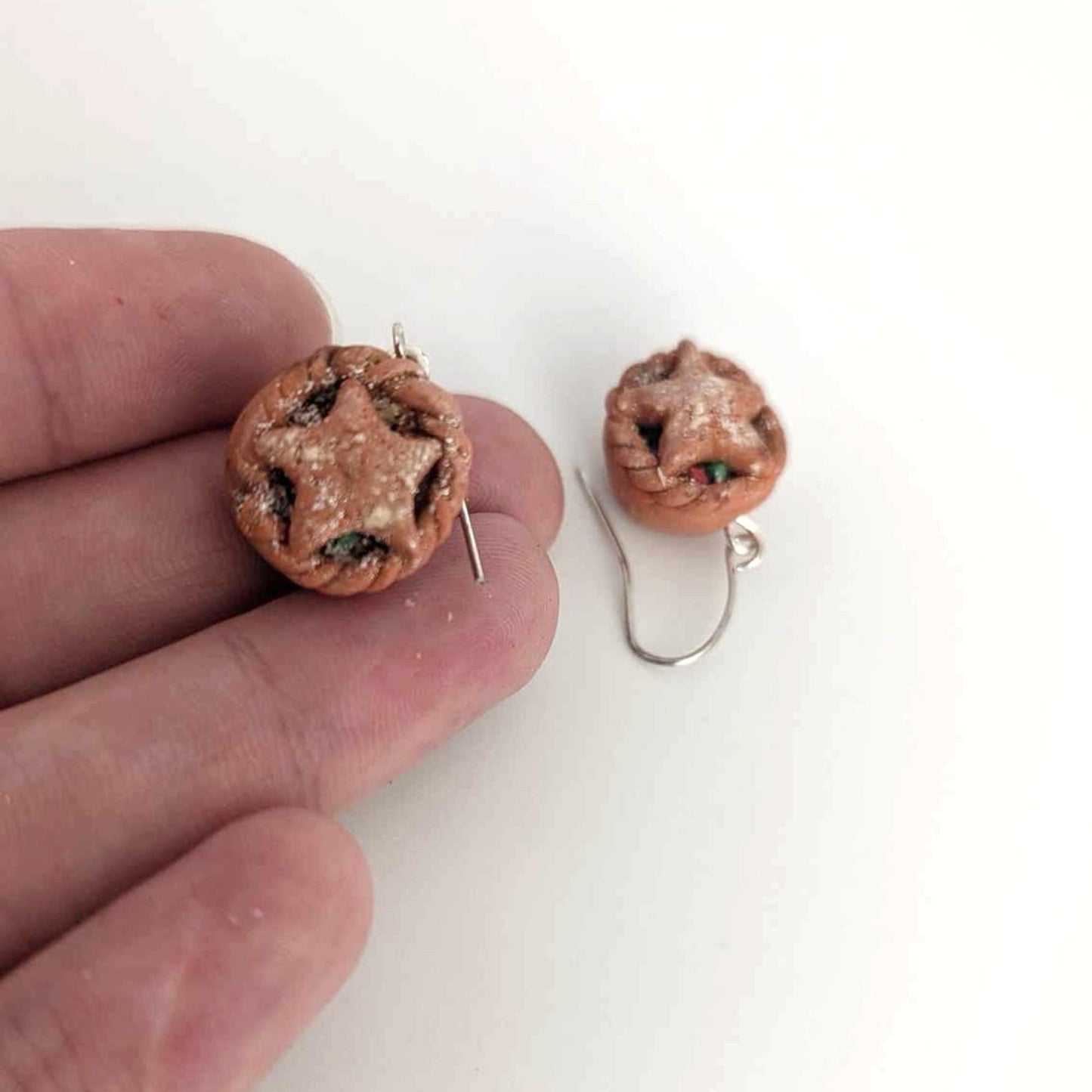 Pair of round earrings with star design held by a hand on a white background