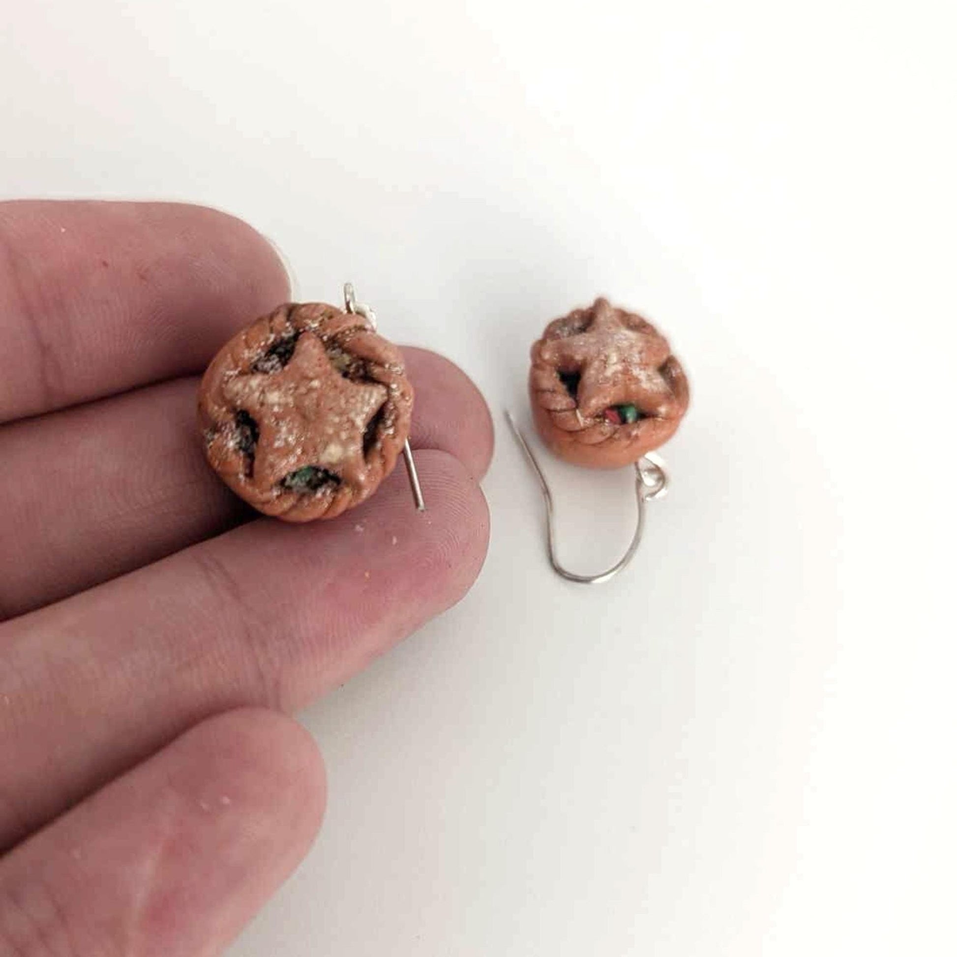 Pair of round earrings with star design held by a hand on a white background