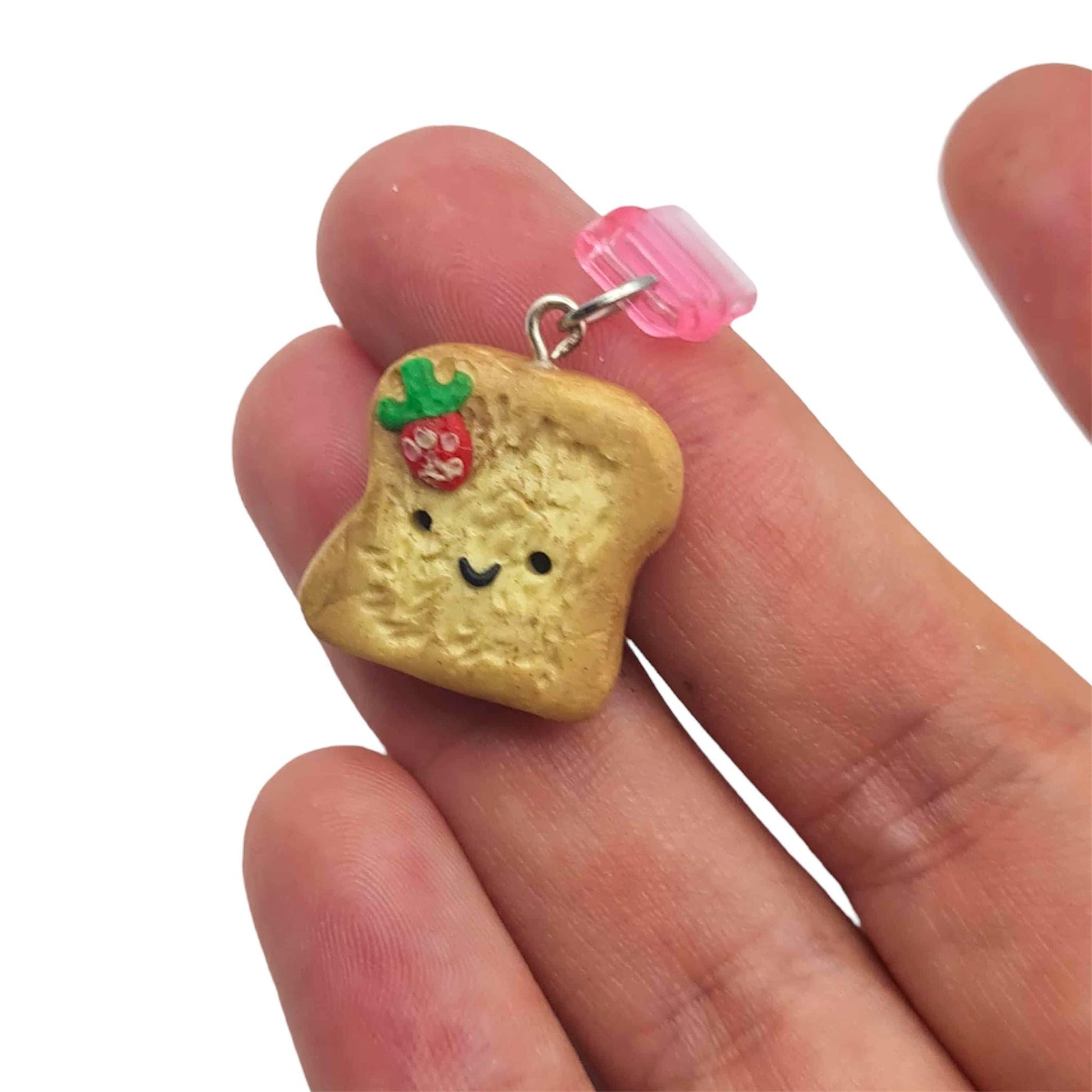 Small bread-shaped charm with a face held between fingers on a white background