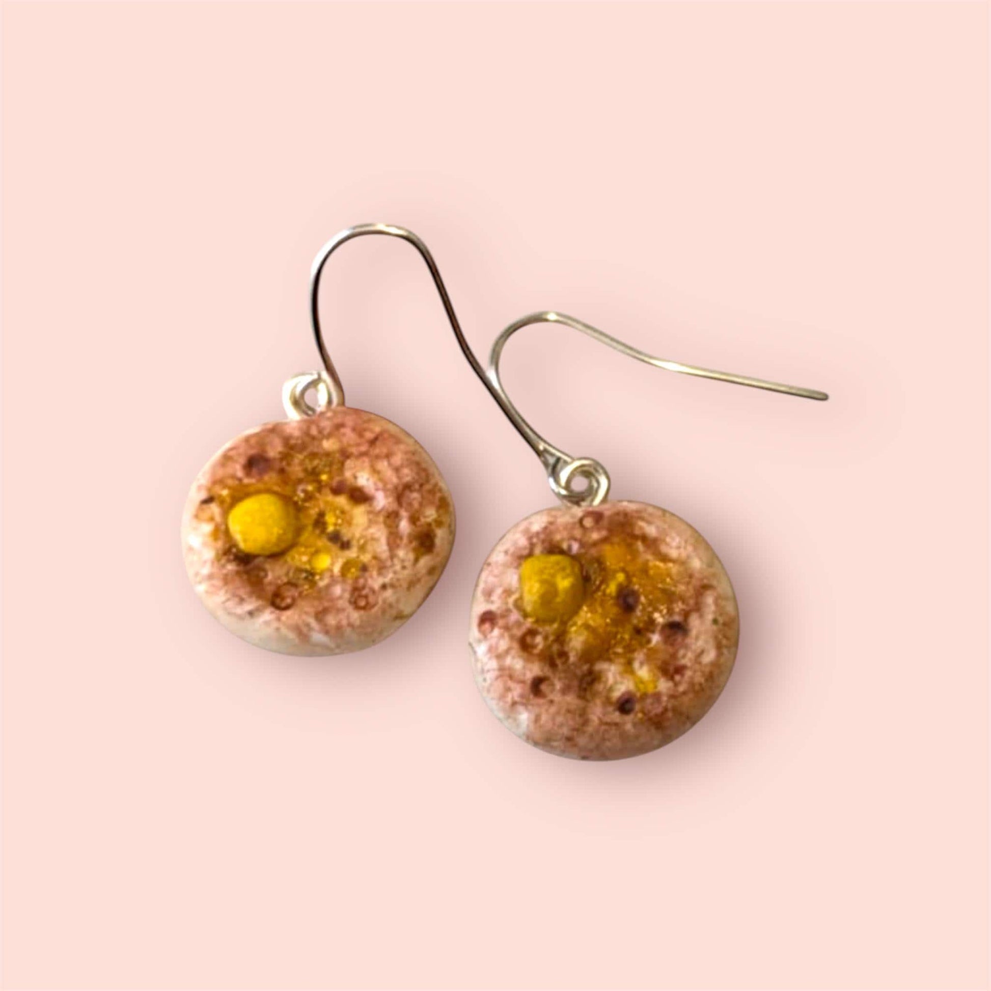 Round earrings with a textured surface and yellow accents on a pink background