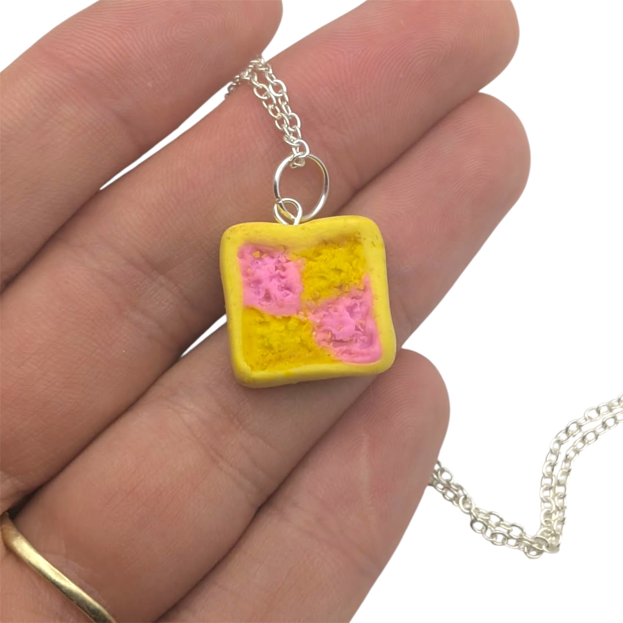 Hand holding a necklace with a square pendant featuring pink and yellow colors.