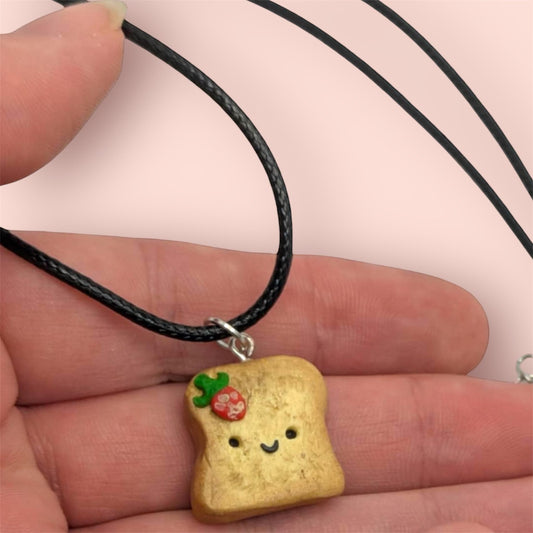 Toast-shaped pendant with a smiling face held in a hand against a light pink background