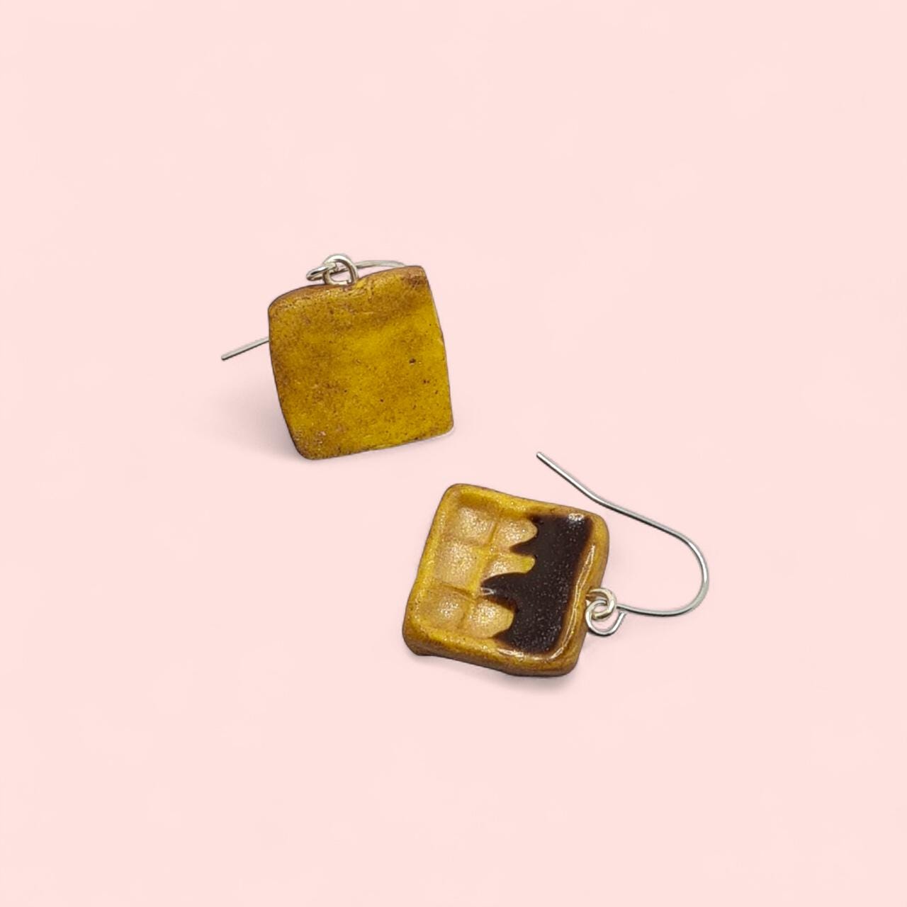 Square earrings with a yellow border and black center on a pink background