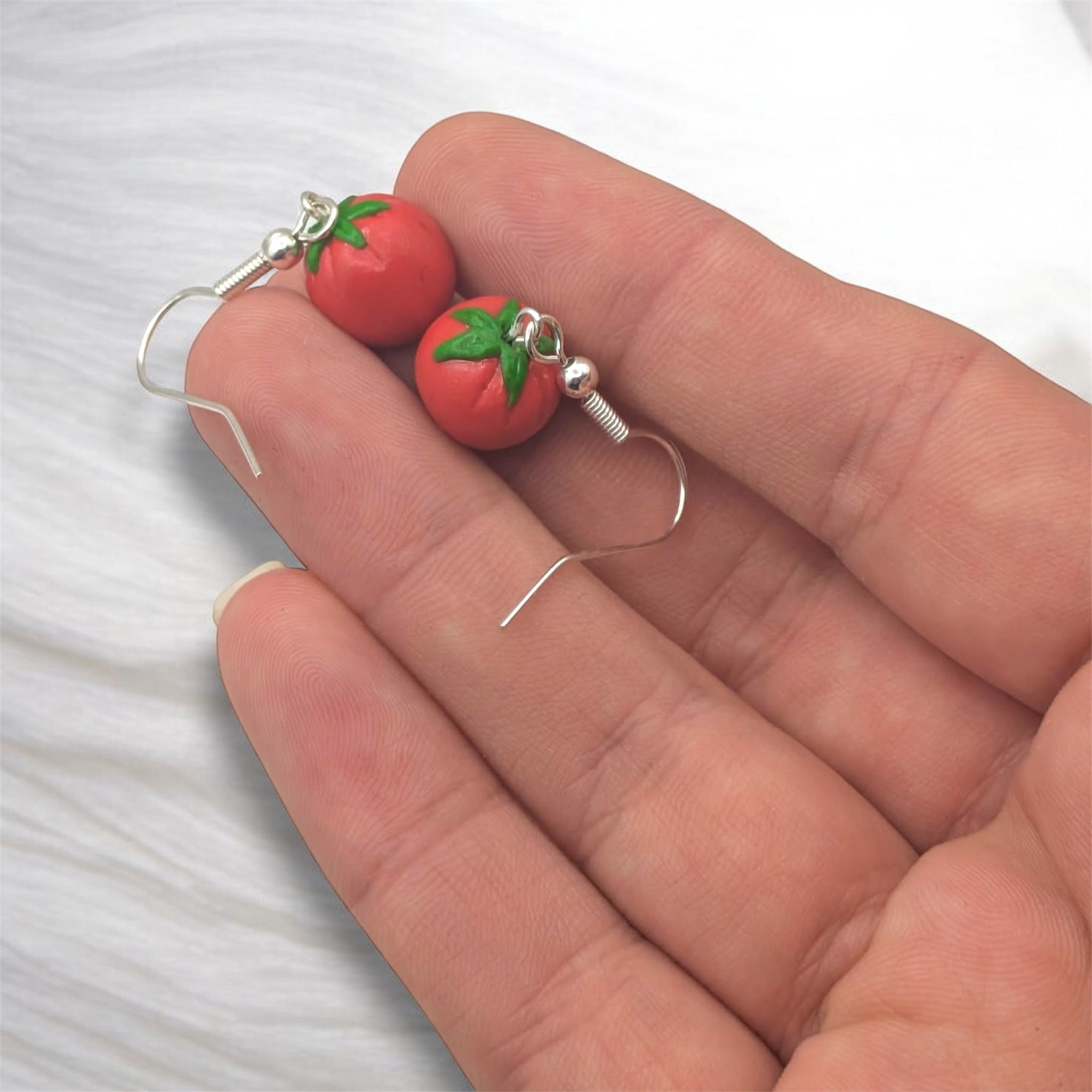 Handmade tomato polymer clay earrings held in hand against a white background