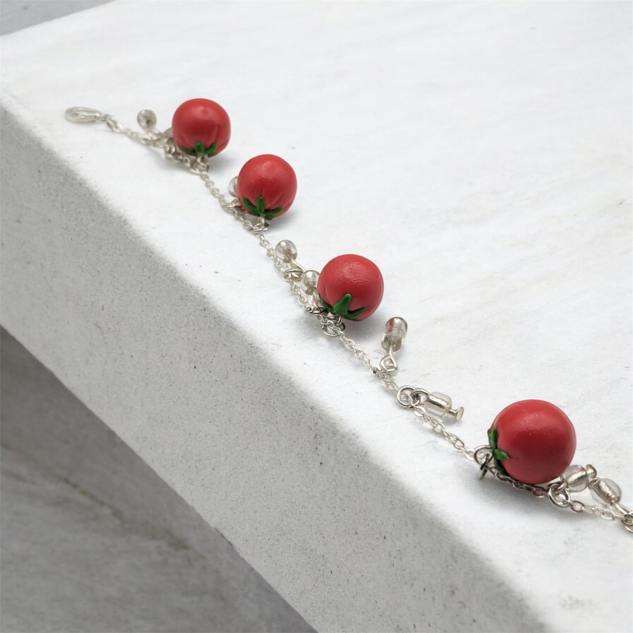 Bracelet with red tomato-shaped polymer clay charms on a white surface
