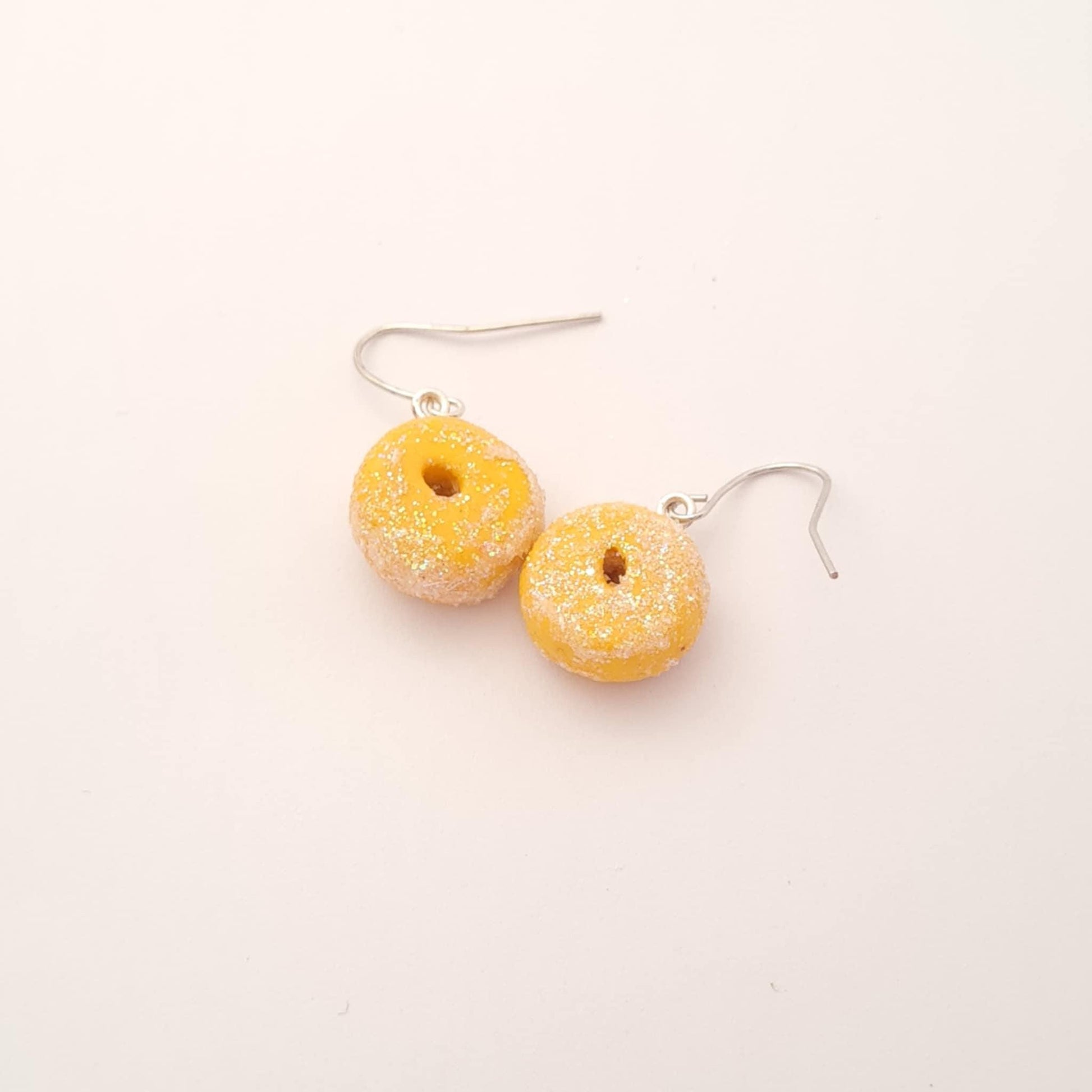 Donut-shaped earrings with yellow glaze and silver hooks on a white background