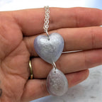 Heart-shaped pendant on a silver chain held in a hand with a marble background