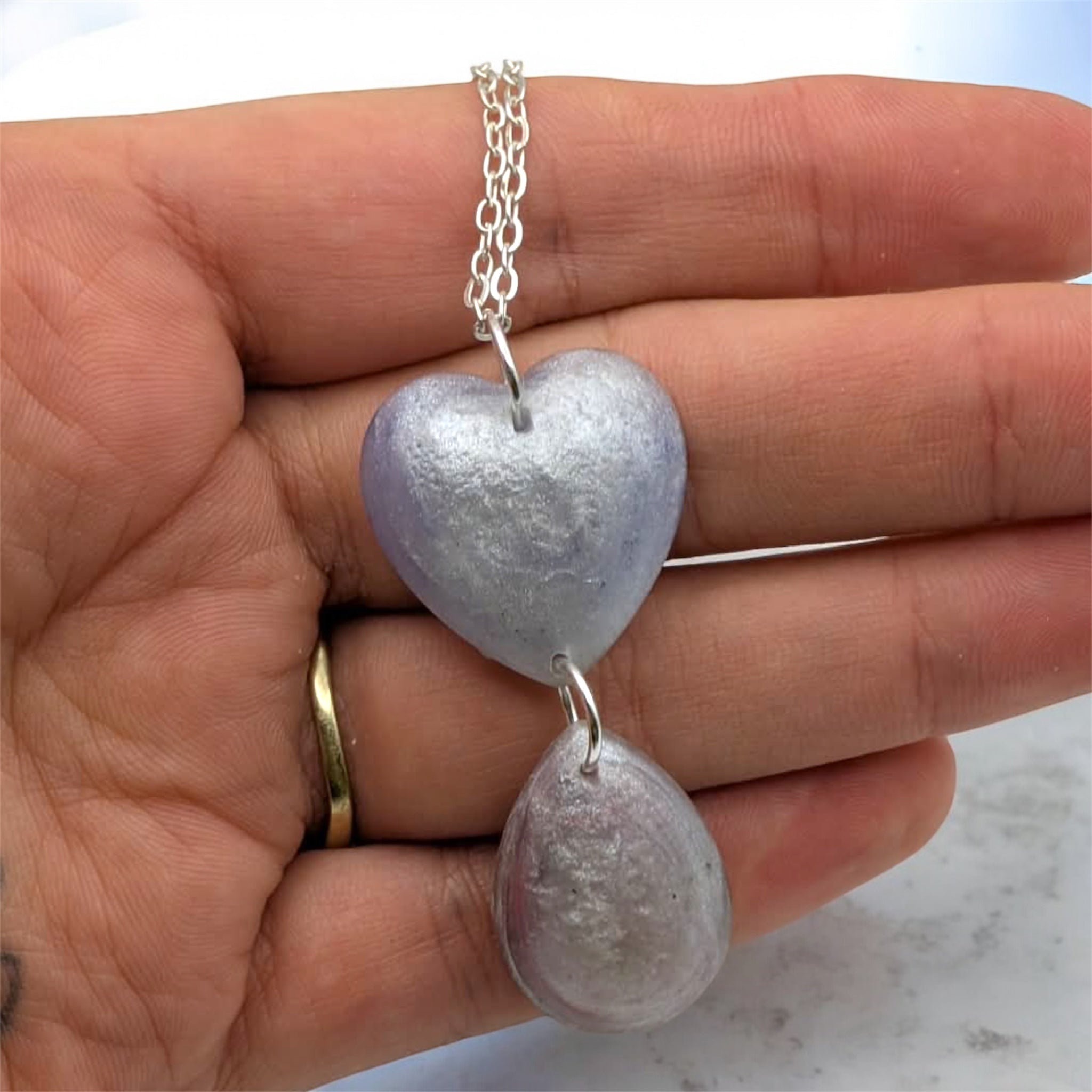 Heart-shaped pendant on a silver chain held in a hand with a marble background