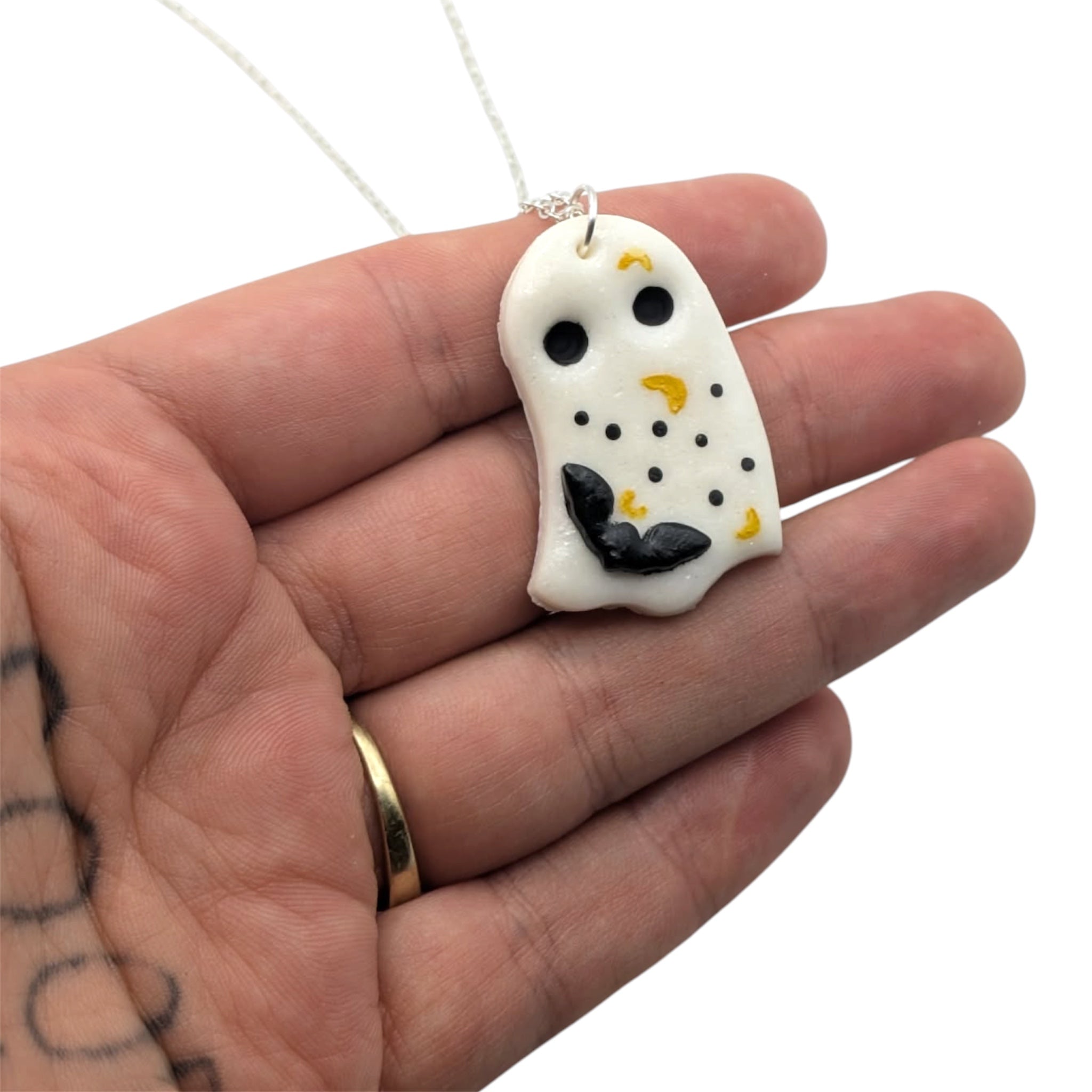 Hand holding a sheet ghost in white with black eyes and bat motif, hand painted spots and moons on silver chain 