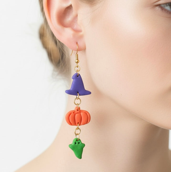 Earrings with purple, orange, and green charms worn by a person on a white background