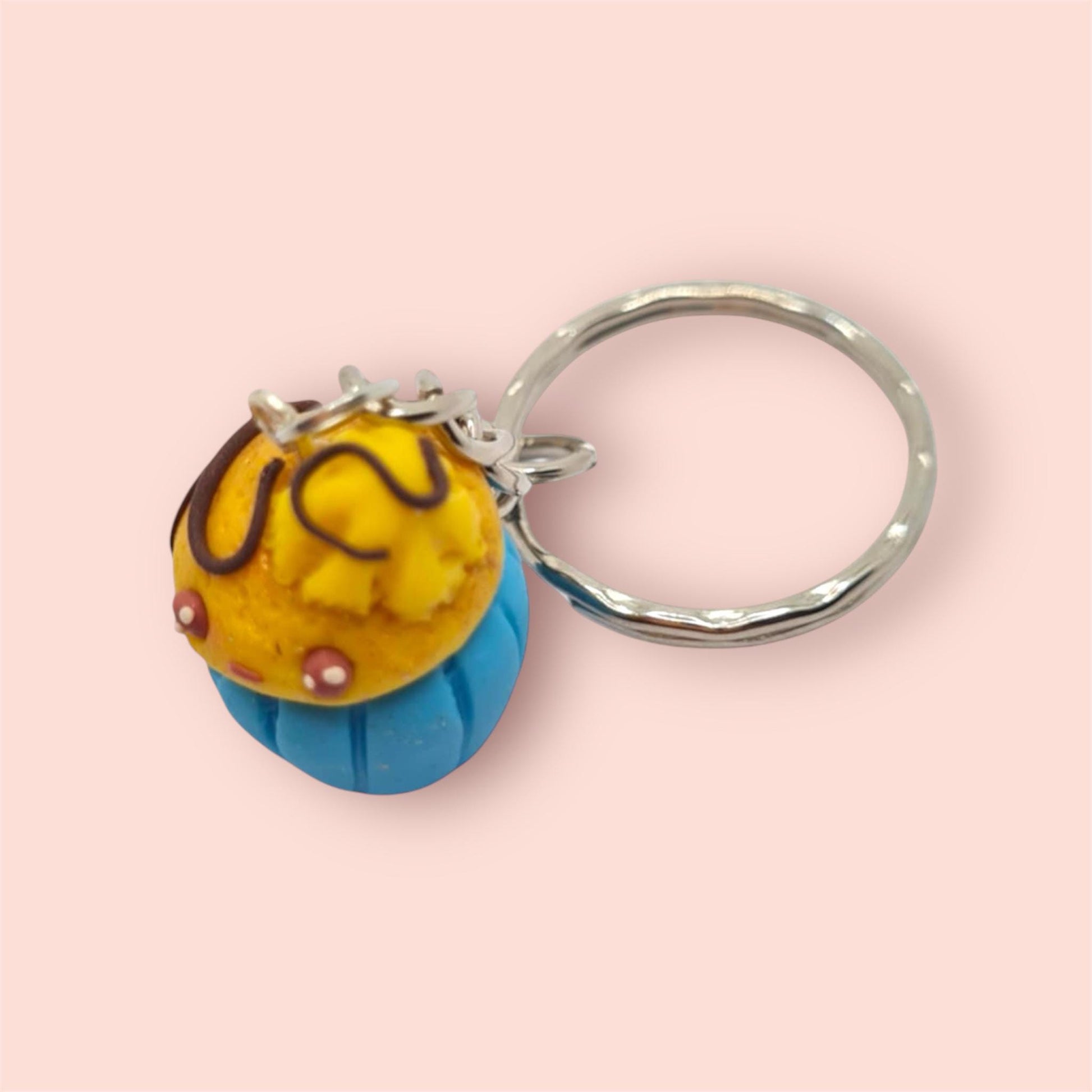 Keychain shaped like a cupcake with yellow filling and blue base on a pink background